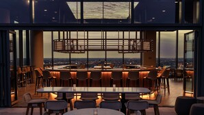 A rooftop bar with a panoramic city view, featuring a mix of bar stools and tables, and a central bar area with a unique lighting fixture. - Hilton Columbus Downtown (Columbus)
