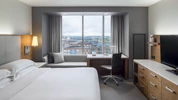 A hotel room with a large bed, a desk, a chair, and a television.