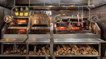 Ett professionellt kök med flera grillar, en vedeldad ugn och ett ställ med ananasfrukter.