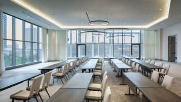 A modern conference room with long tables and chairs, large windows offering city views, and contemporary lighting fixtures.