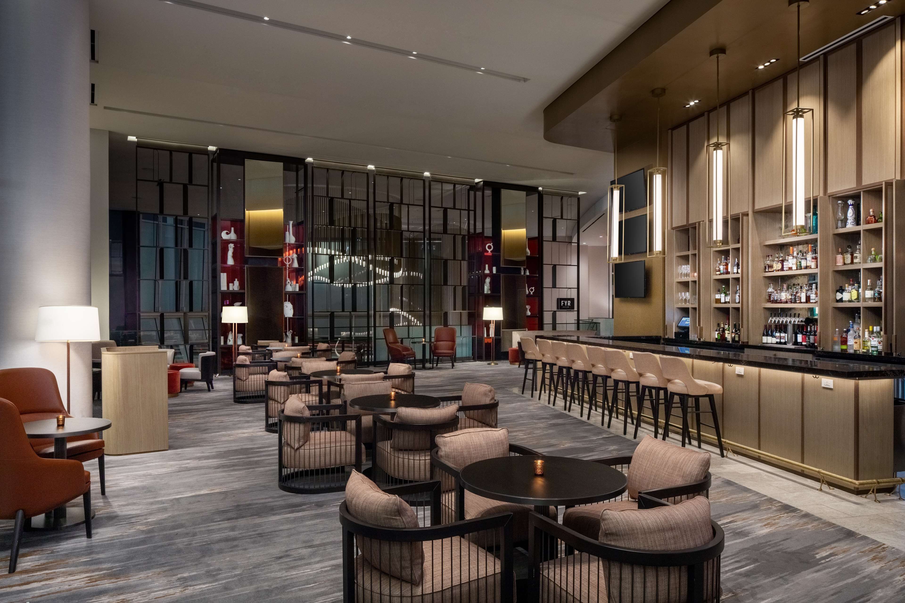 A modern hotel lobby with a bar area, seating arrangements, and a large screen.
