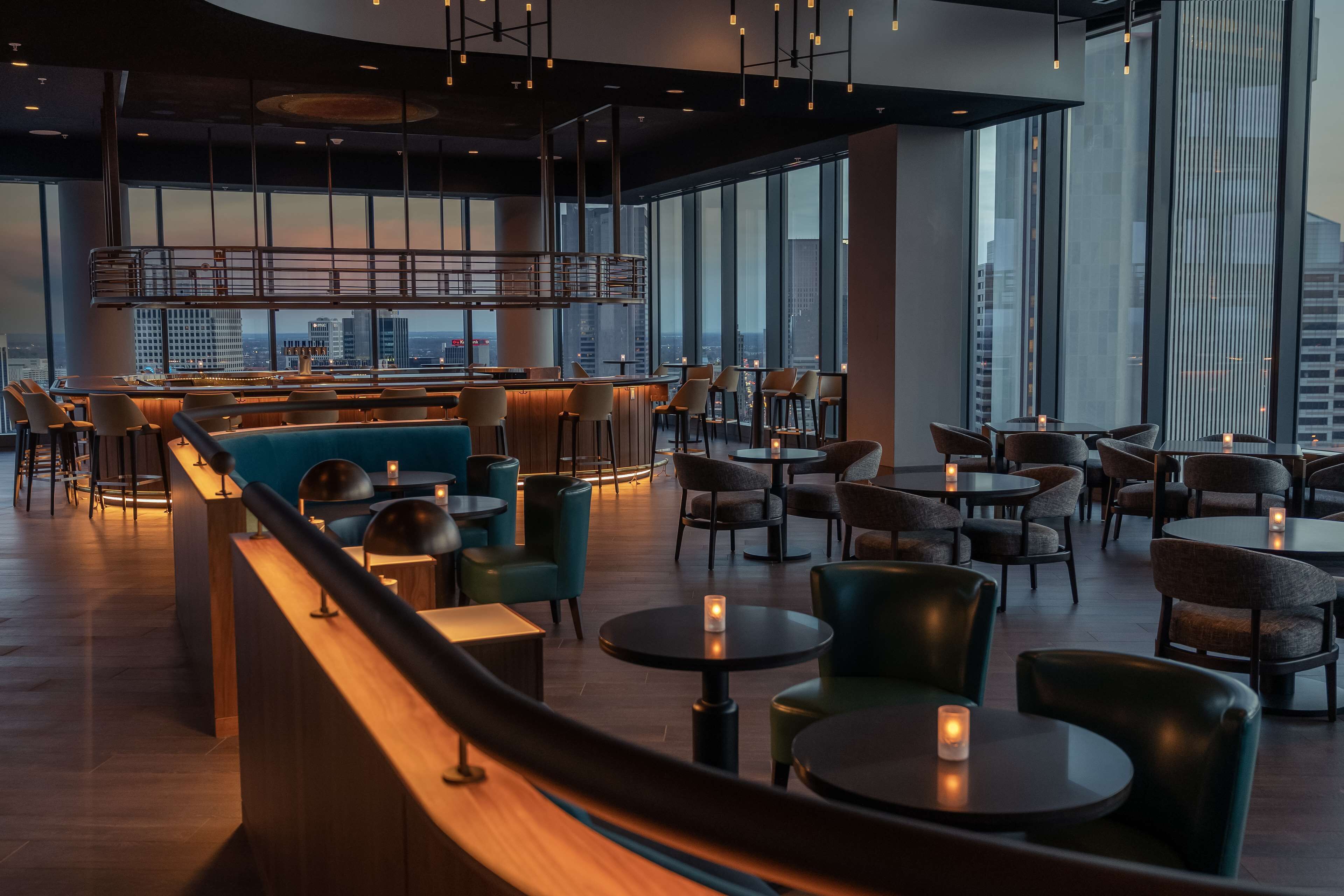 Zona de bar moderna con asientos, ventanas amplias y vista a la ciudad.