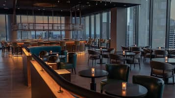 Zona de bar moderna con asientos, ventanas amplias y vista a la ciudad.
