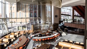 A modern restaurant with a central bar, multiple seating areas, and large windows offering views of the city. - Hilton Columbus Downtown (Columbus)
