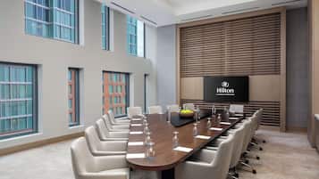 A conference room with a long table, white chairs, and a large screen displaying the Hilton Columbus Downtown logo.