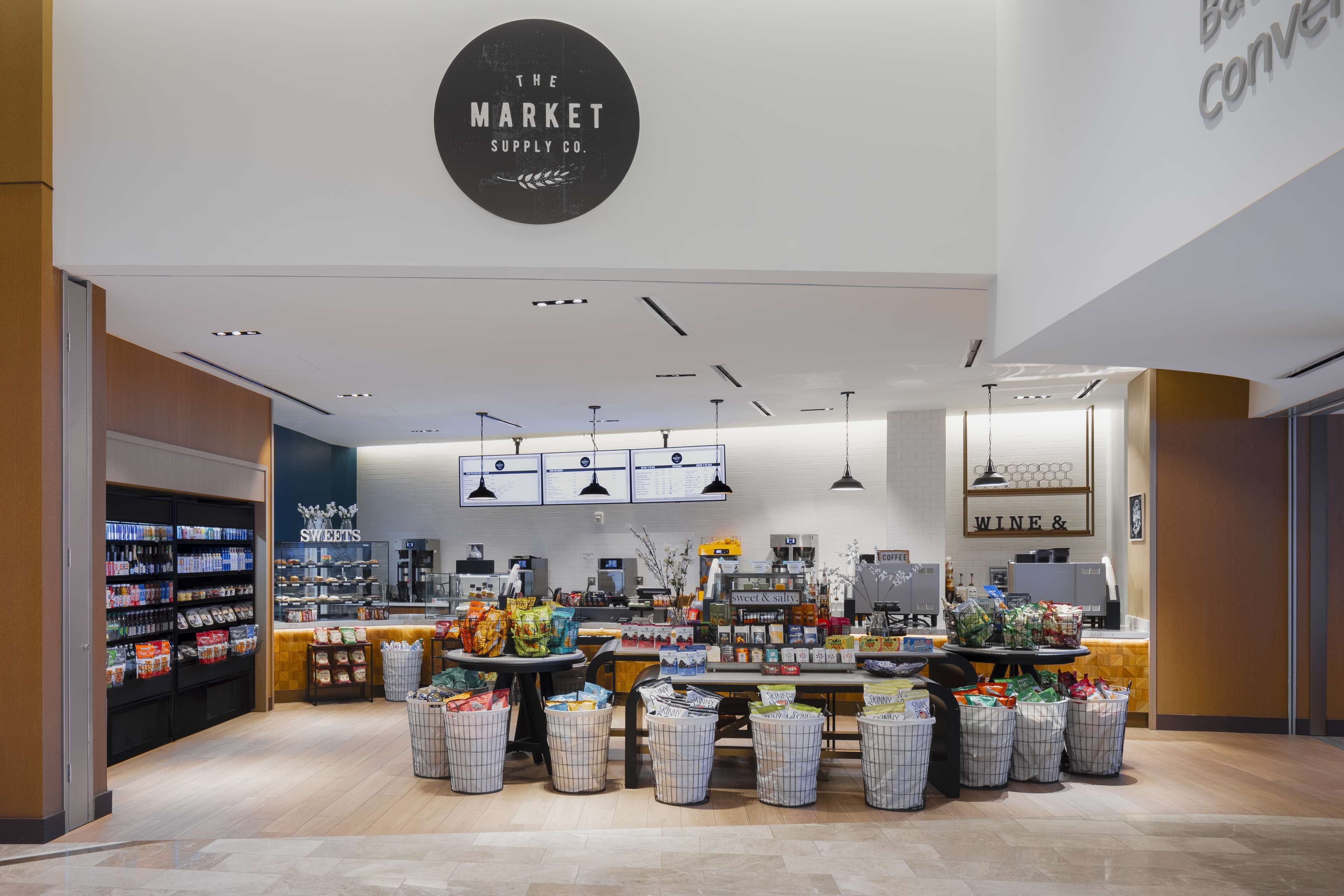 A modern retail store with a central checkout counter, shelves stocked with products, and a sign indicating a wine section.