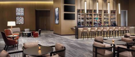 Un espace lounge moderne avec des tables rondes et des fauteuils confortables, un bar avec des étagères remplies de bouteilles et un téléviseur fixé au mur.