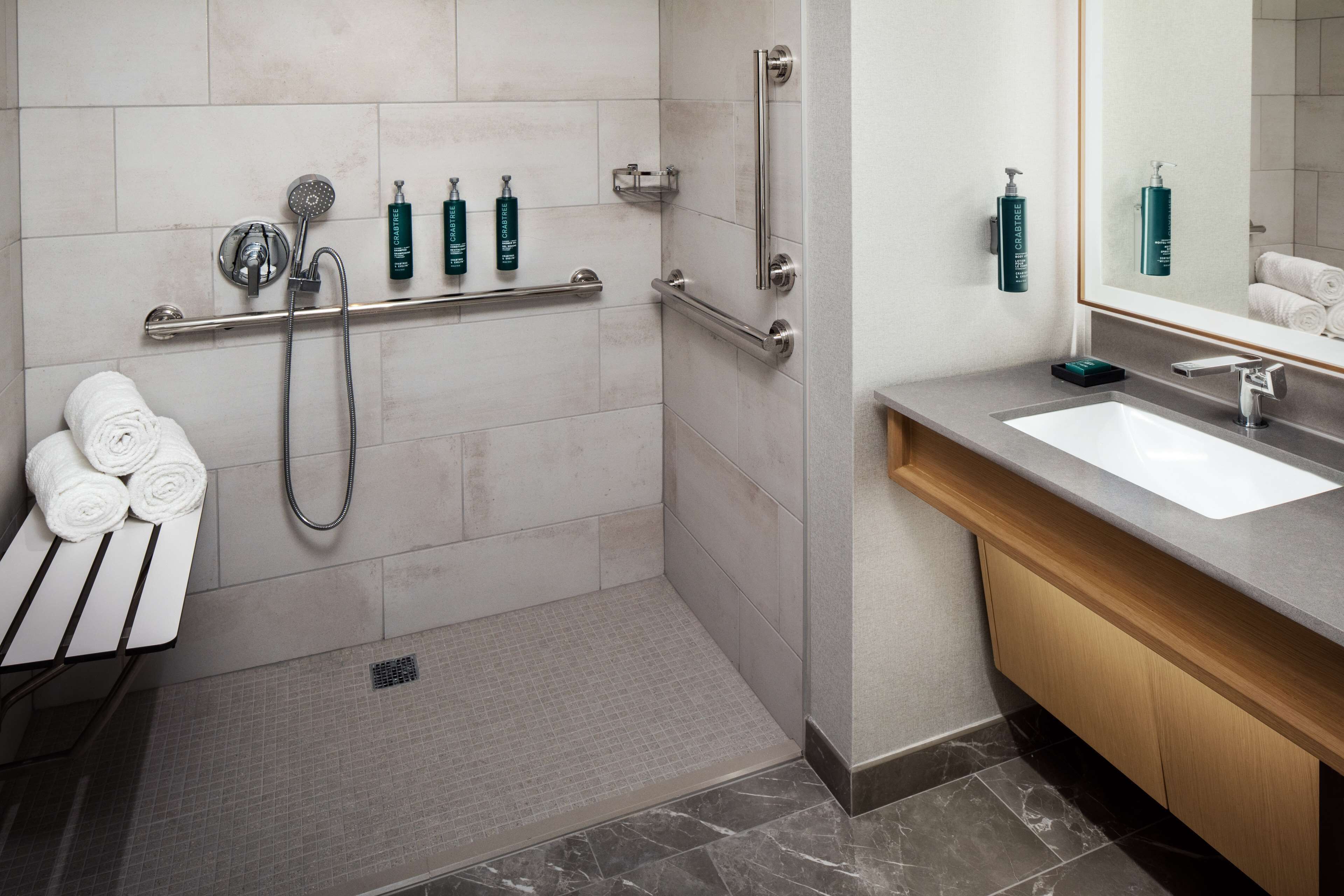 Un baño moderno con cabina de ducha a ras, barras de apoyo, lavamanos y perchero.