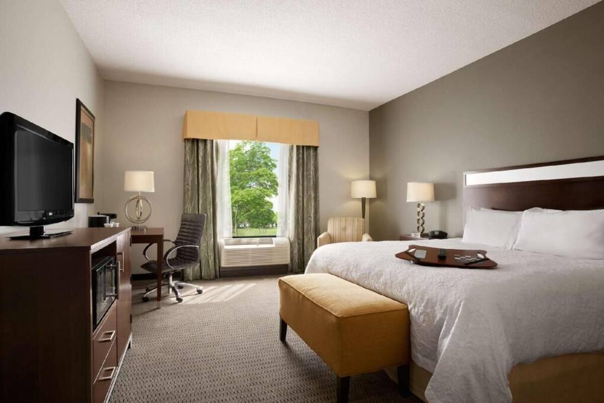 Habitación de hotel con cama, televisión, escritorio, silla y ventana con cortinas.