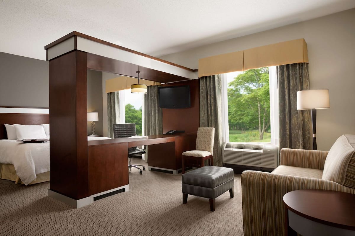 Ein Hotelzimmer mit Bett, Schreibtisch, Stuhl, Hocker und Fernseher.
