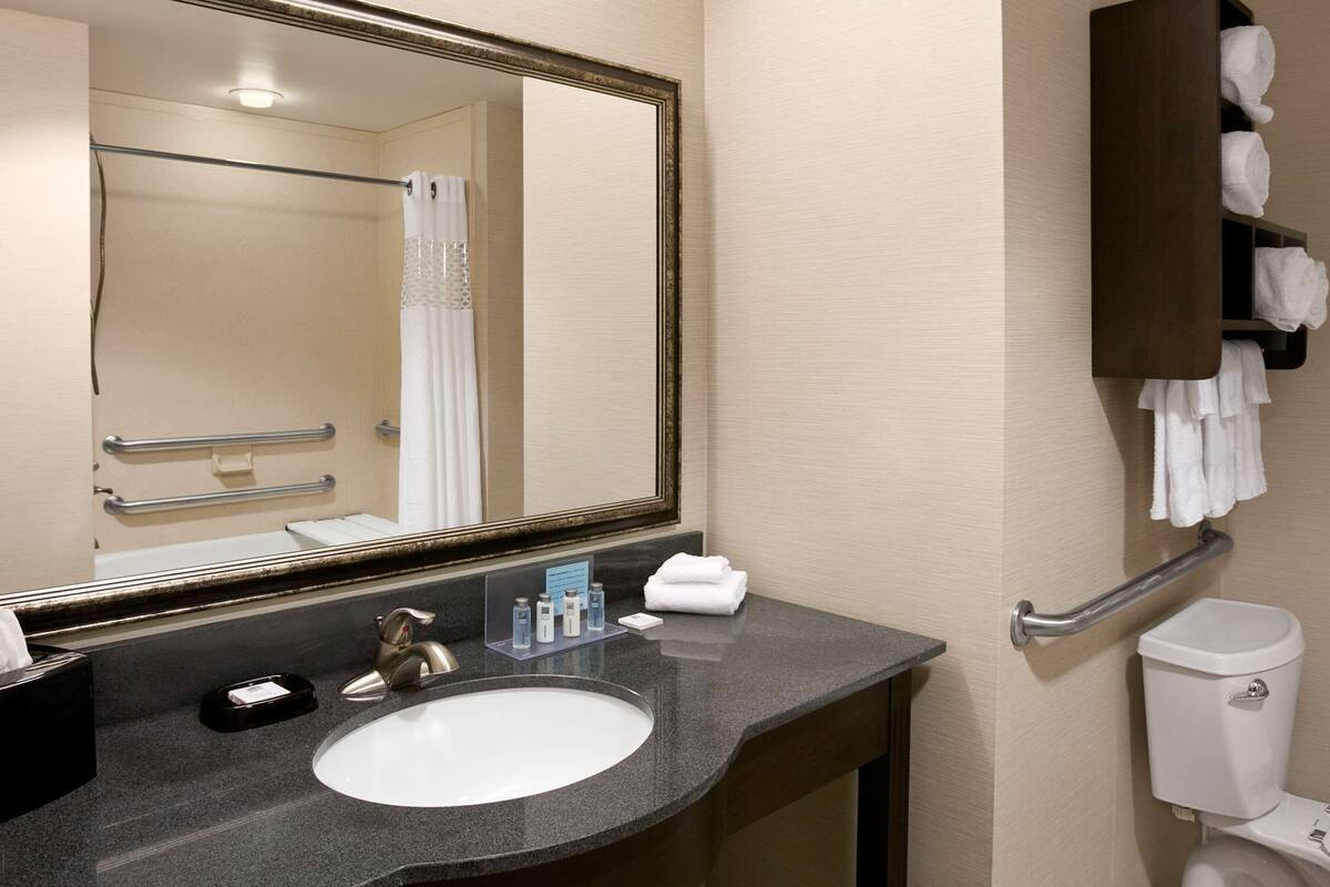 Ein Badezimmer mit Waschbecken, Spiegel, Handtuchhalter und Toilette.