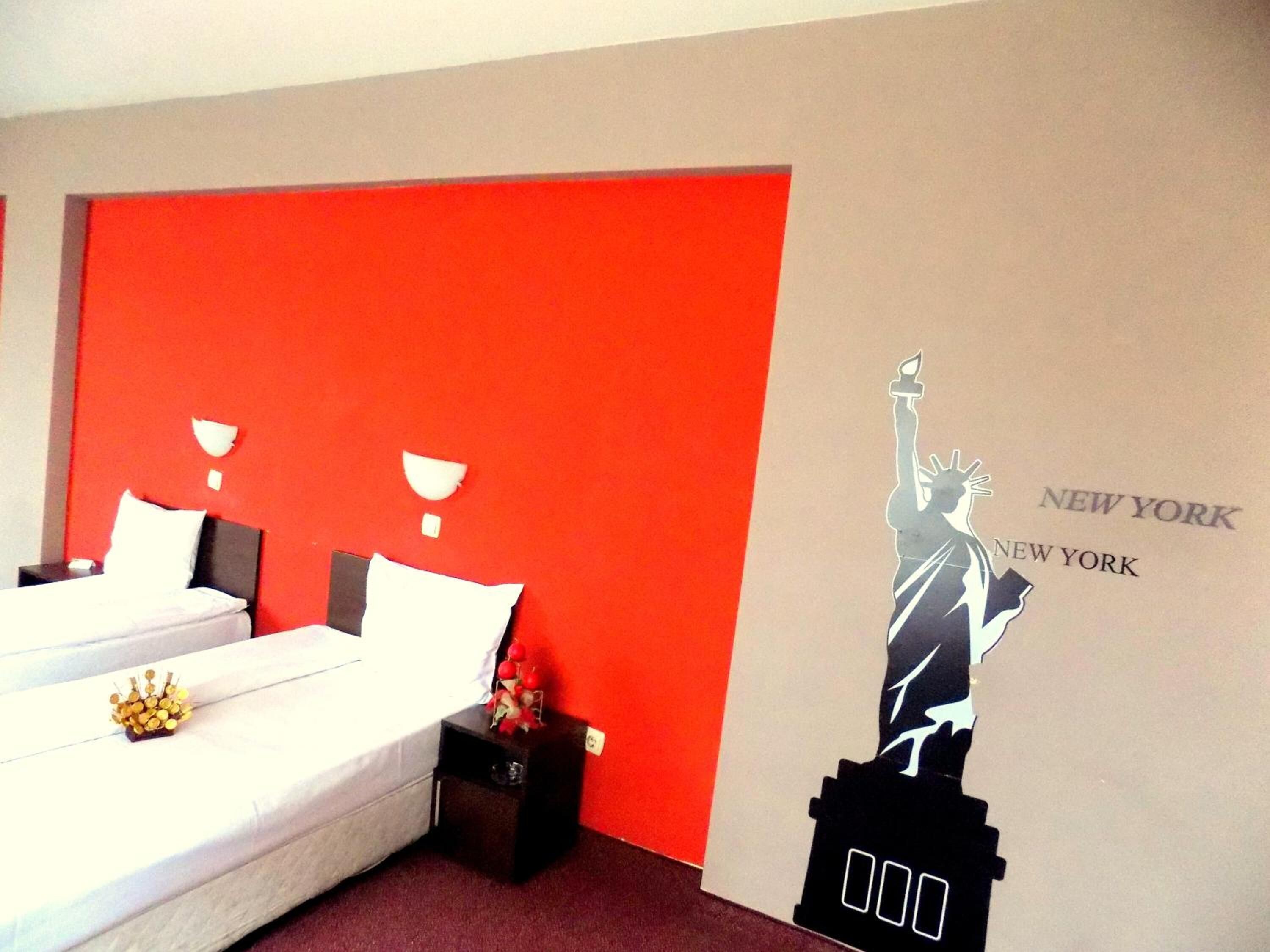 A hotel room with a large bed, a nightstand, and a wall with a New York City skyline mural.
