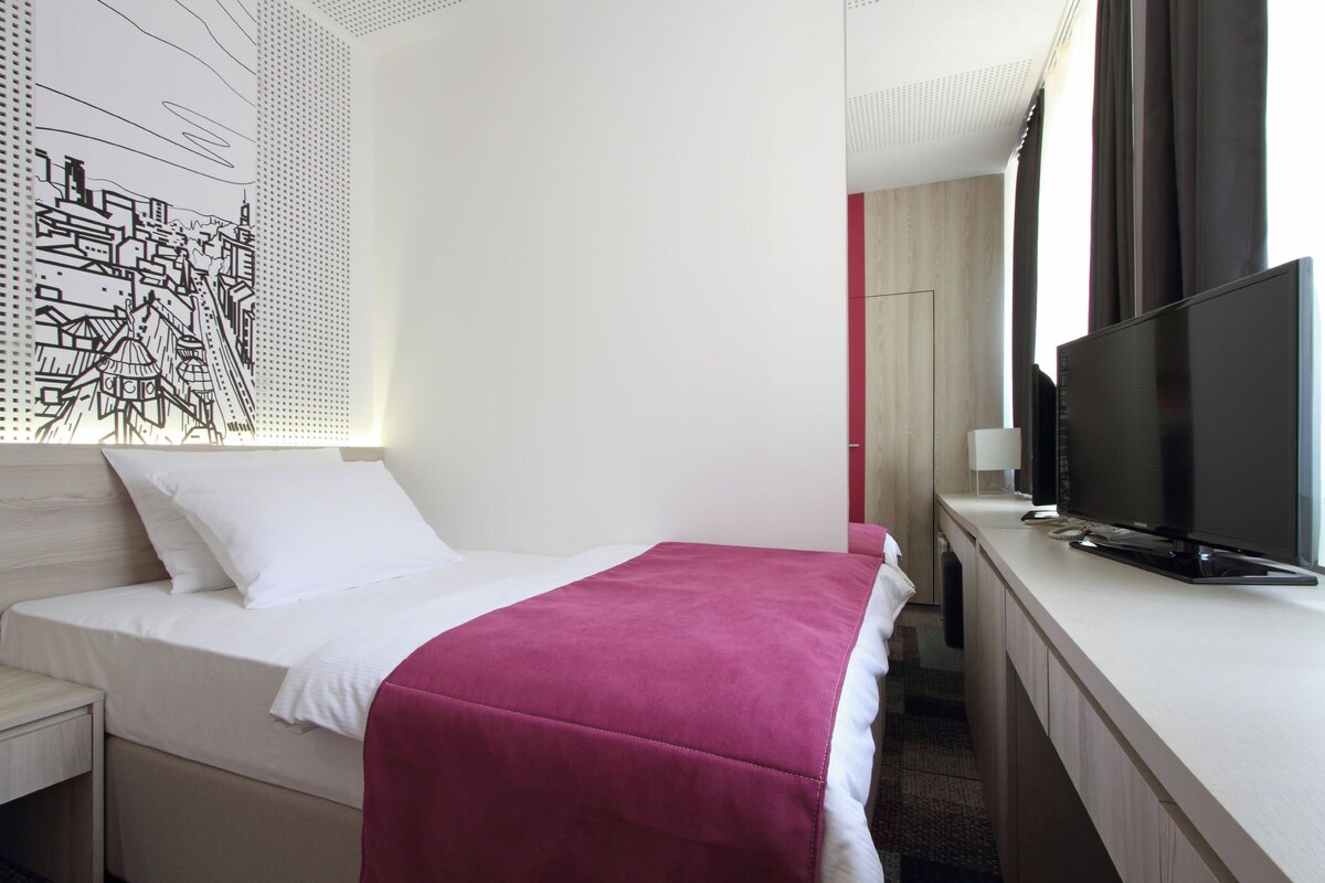 A hotel room with a bed, a TV, and a wall art piece.