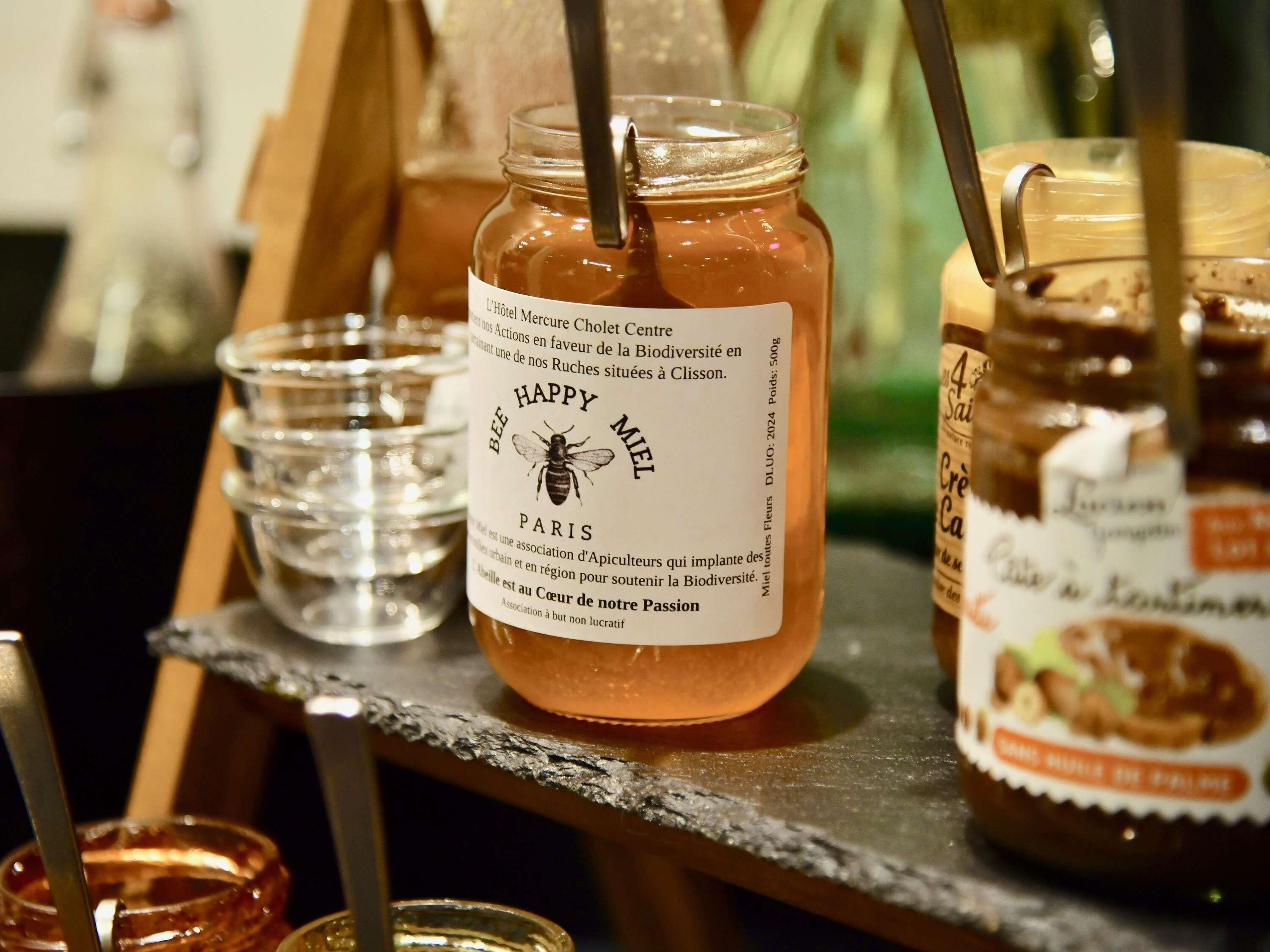 A jar of honey with a label, a glass, and a jar of jam on a table.