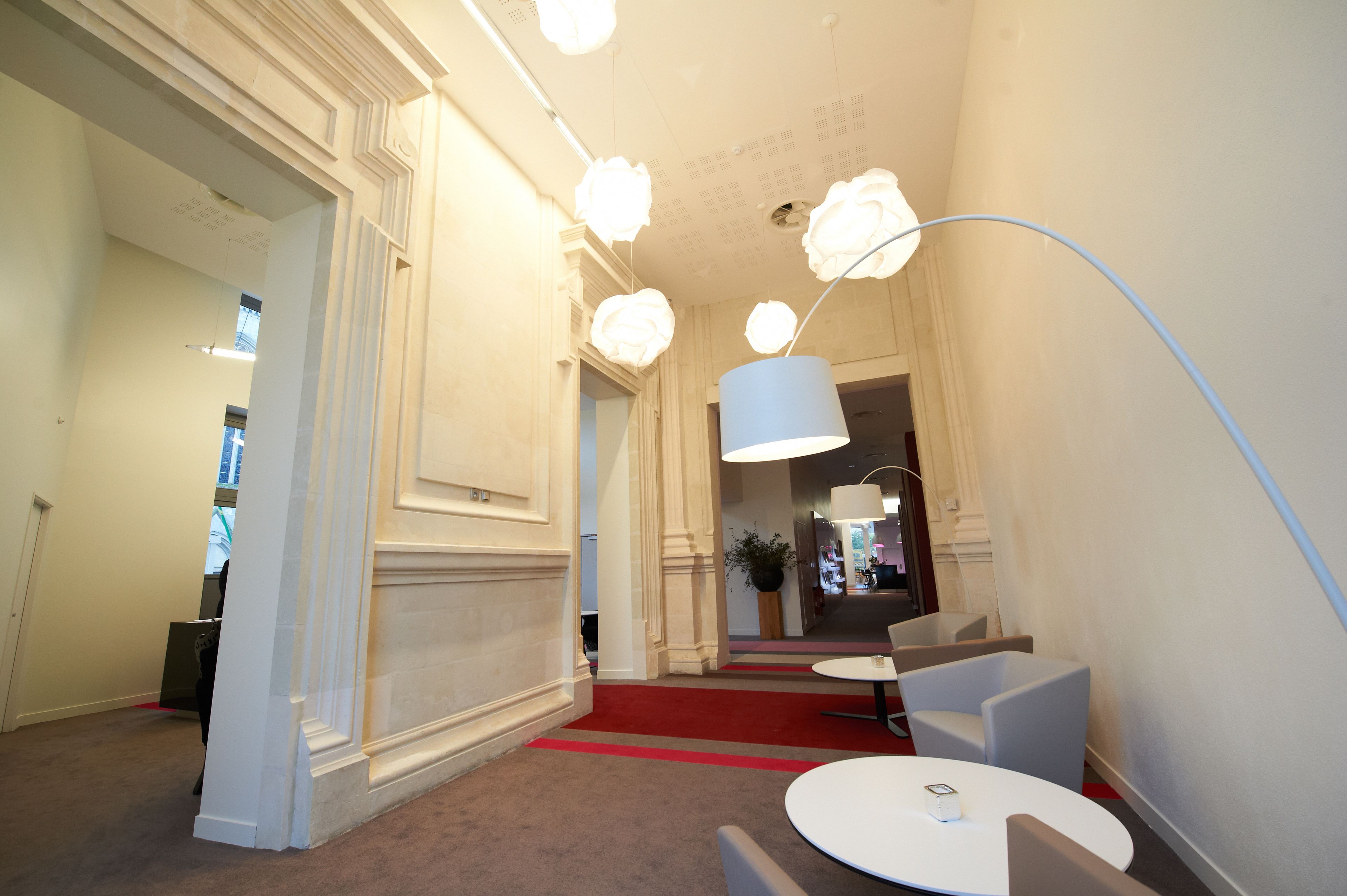 A hotel lobby with a red carpet, white walls, and a modern chandelier.