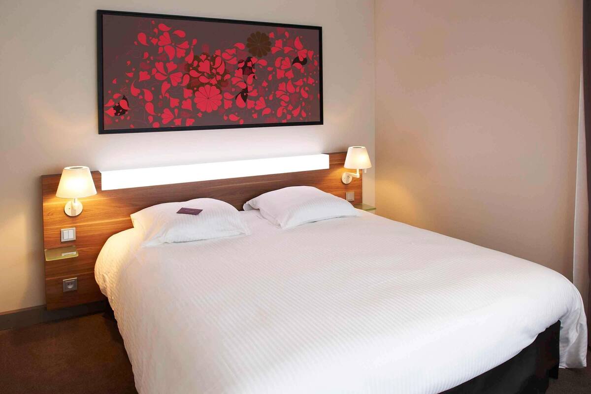 A hotel room with a large bed, two bedside lamps, a nightstand, and a wall-mounted artwork.