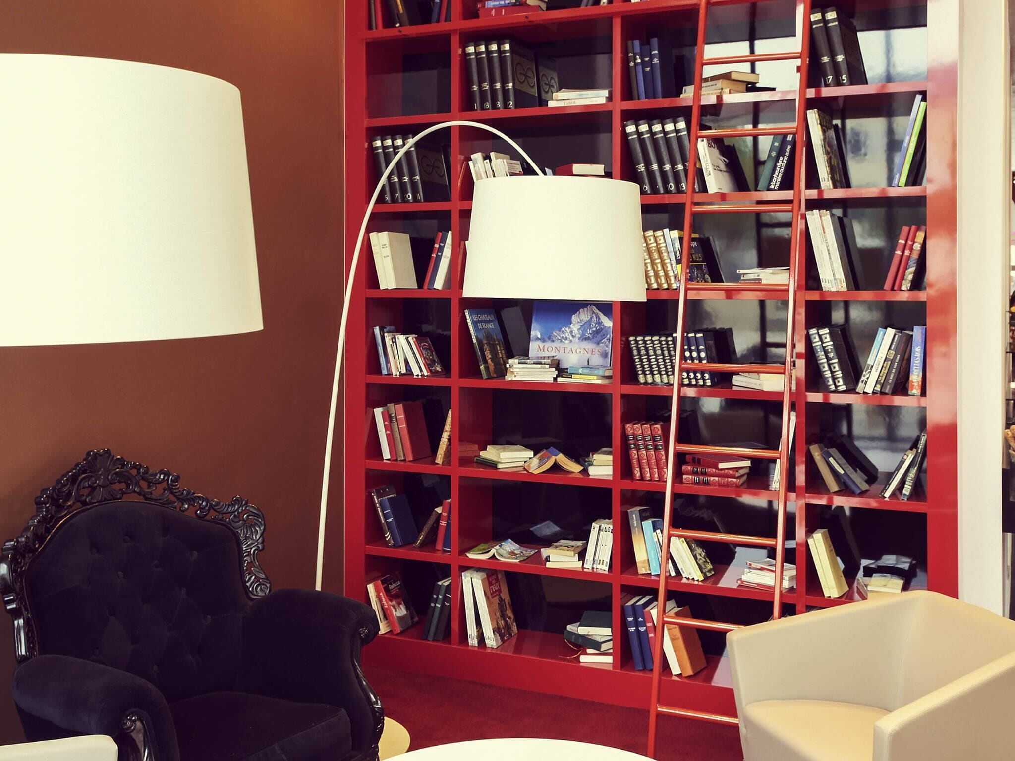 Una biblioteca con una estantería roja, una lámpara blanca y dos sillas.