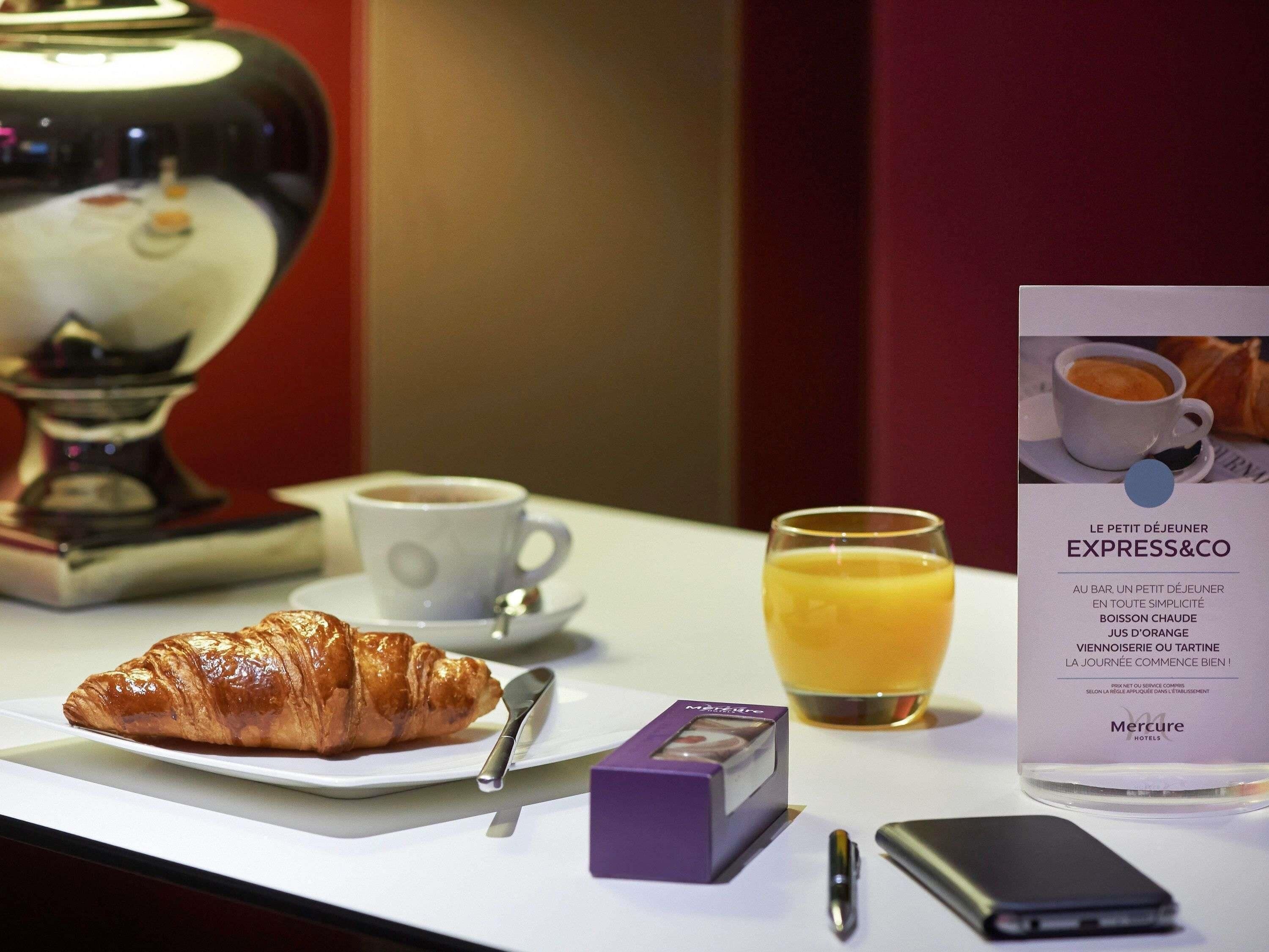 Um café da manhã com um croissant, café e suco de laranja sobre a mesa.