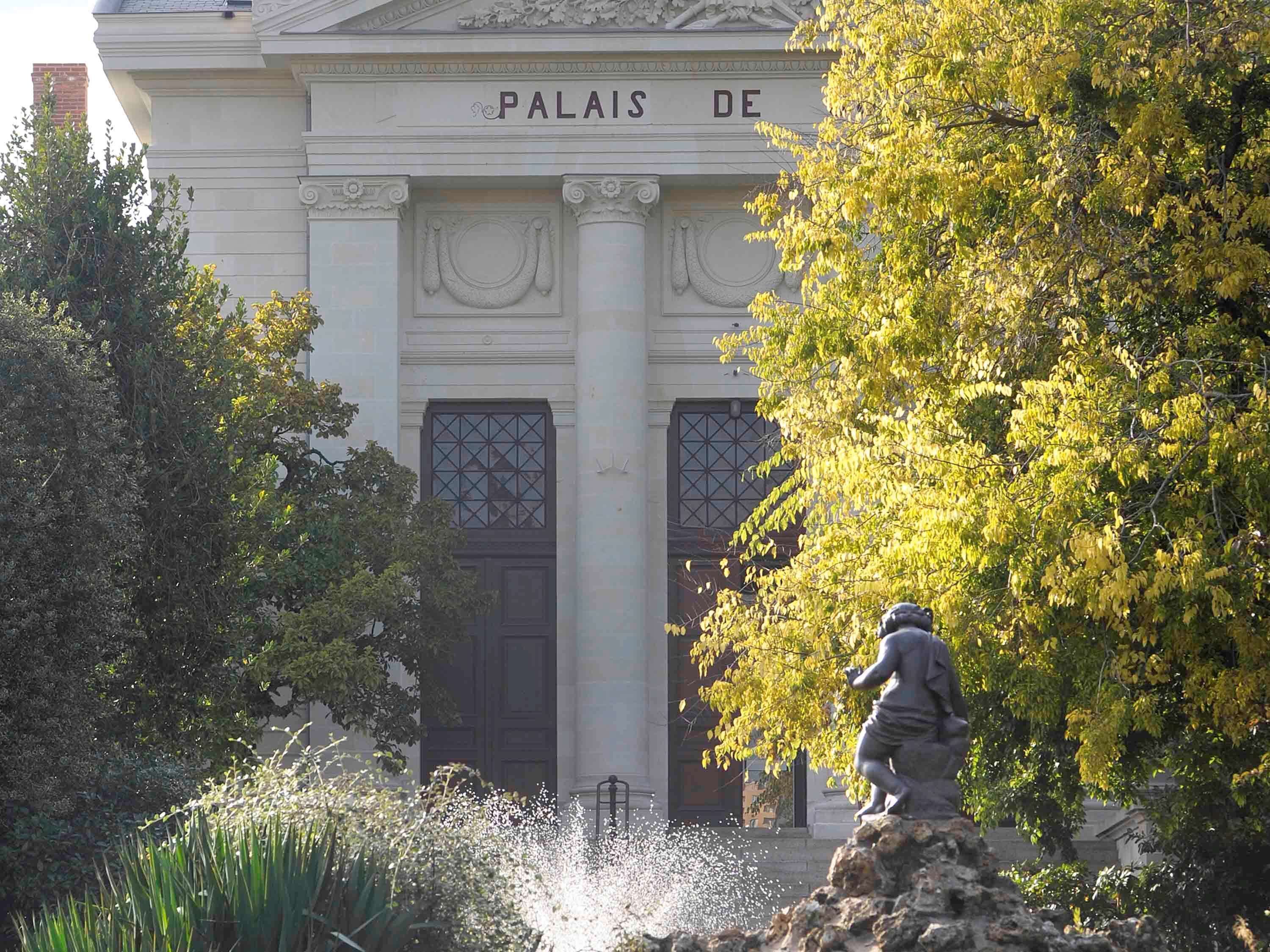 Ein Gebäude mit der Aufschrift "PALAISE DE" auf der Fassade, umgeben von Bäumen und einer Statue.