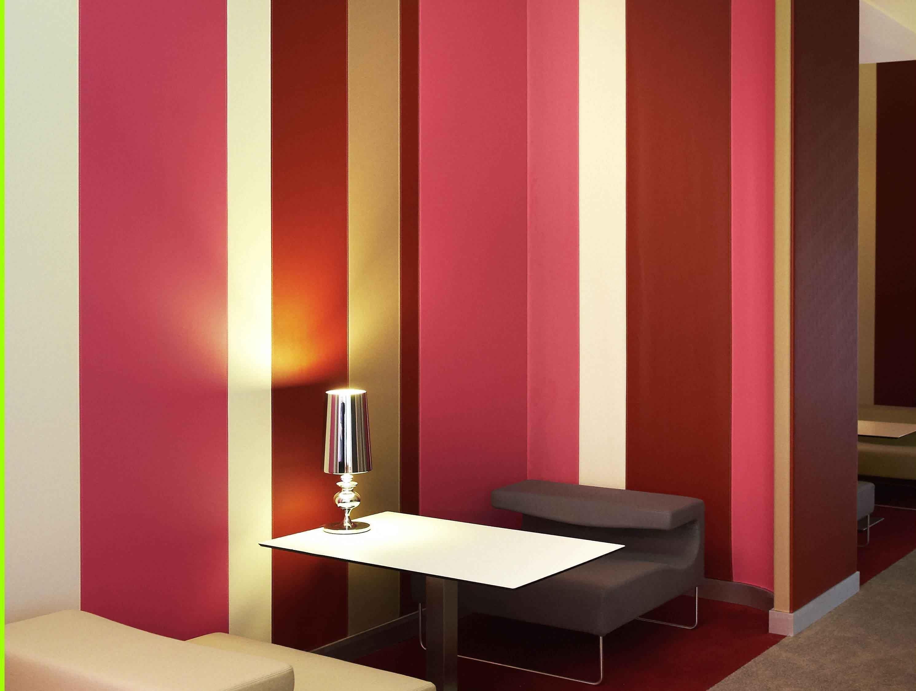 A modern room with a white table and a grey bench against a wall with vertical stripes in red, beige, and brown.