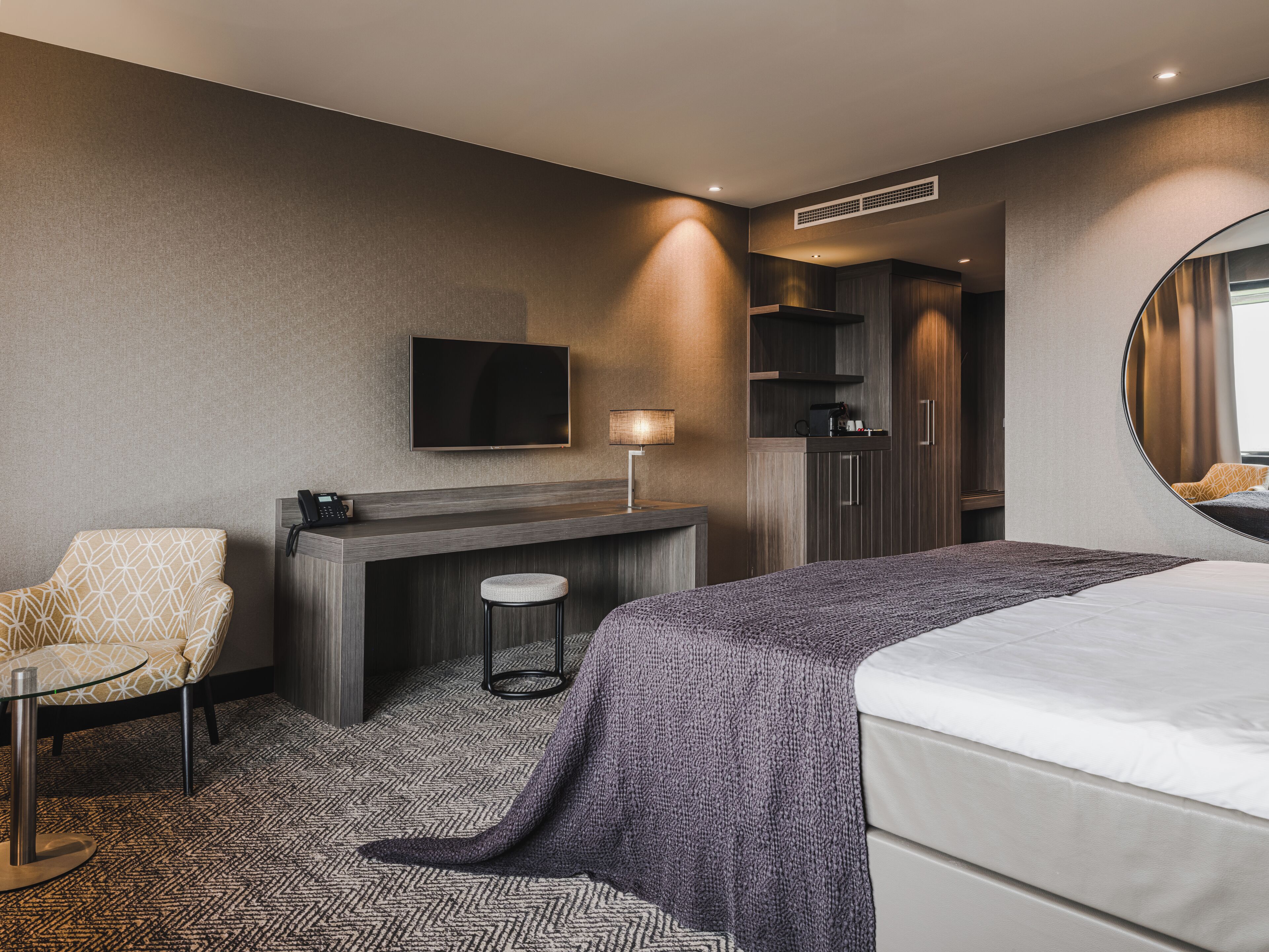 Une chambre d’hôtel moderne équipée d’un lit, d’un bureau, d’une chaise, d’une télévision et d’un miroir.