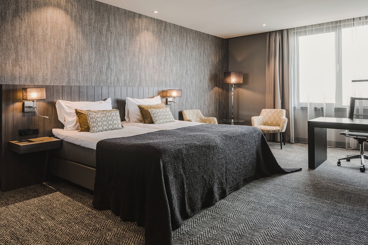 Moderni hotellihuone, jossa on suuri sänky, kaksi yöpöytää, työpöytä ja tuoli.