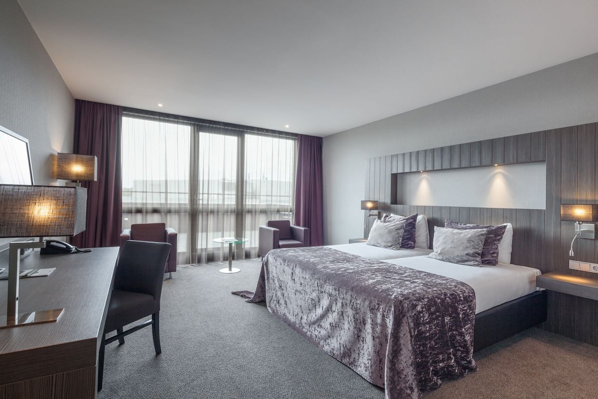 Hotellihuone, jossa on sänky, työpöytä, tuoleja ja näkymä kaupunkiin.