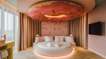 Een moderne slaapkamer met een rond bed, een groot kunstwerk aan het plafond en een aan de muur bevestigde televisie.