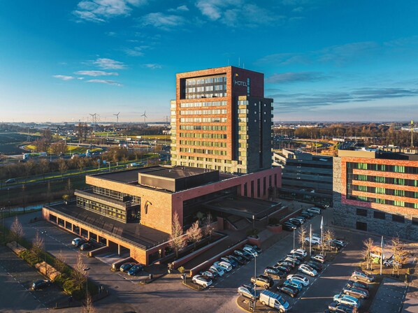 A modern hotel with a prominent tower, a parking lot, and a view of the surrounding area.