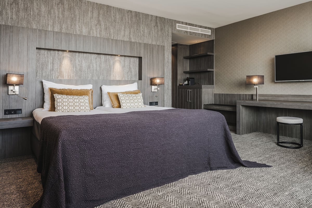 Moderni hotellihuone, jossa on suuri sänky, yöpöydät, työpöytä ja televisio.