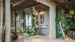 Een moderne badkamer met een douchecabine van glas, een houten plafond en een groene wand met planten.