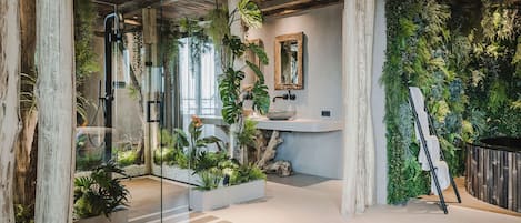 Un baño moderno con cabina de ducha de vidrio, techo de madera y pared verde con plantas.