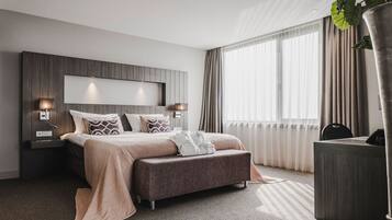 Una habitación de hotel moderna con una cama grande, lámparas de noche, un escritorio y una planta en maceta.