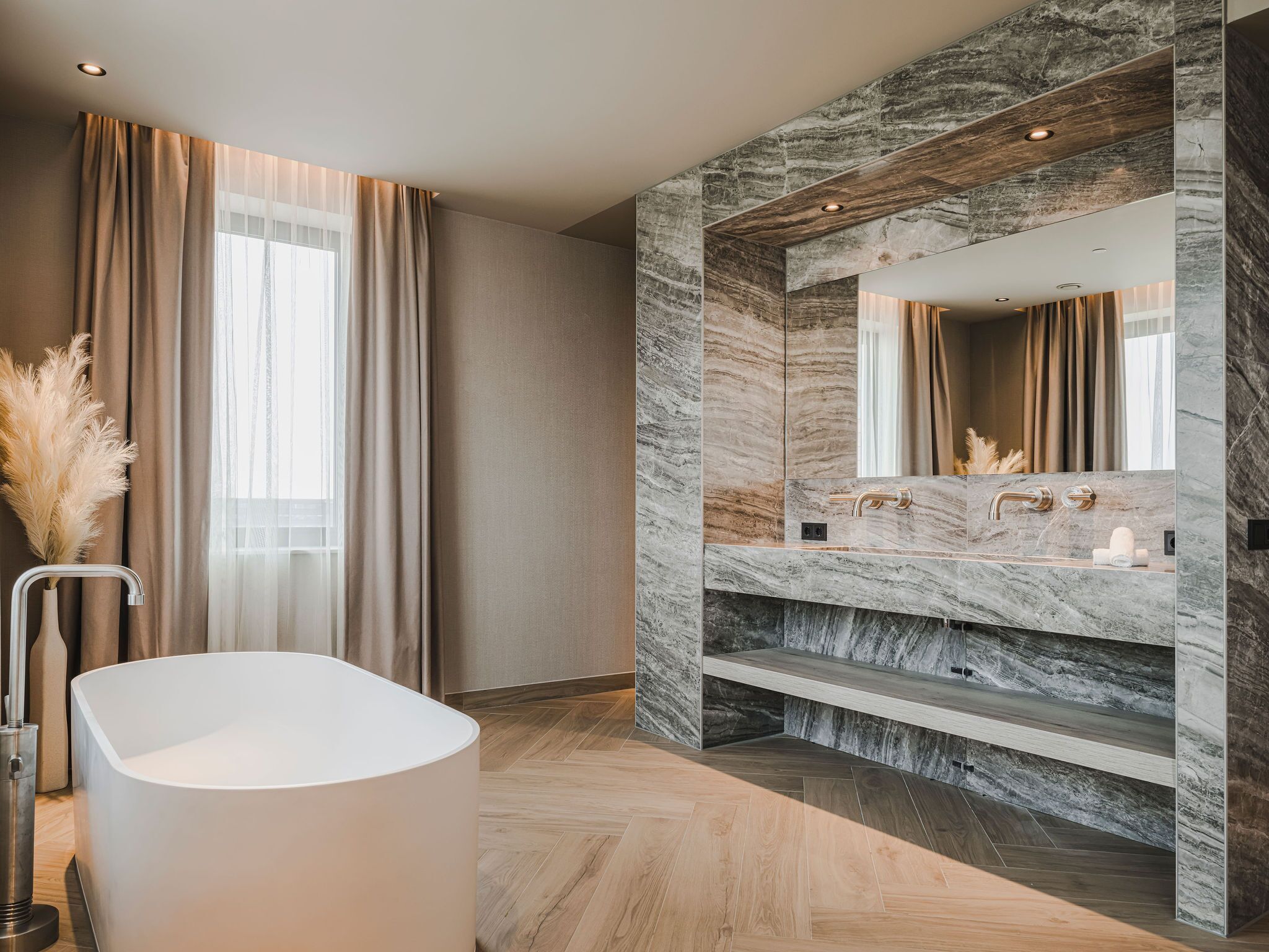 A modern bathroom with a freestanding bathtub, marble walls, and a large mirror.