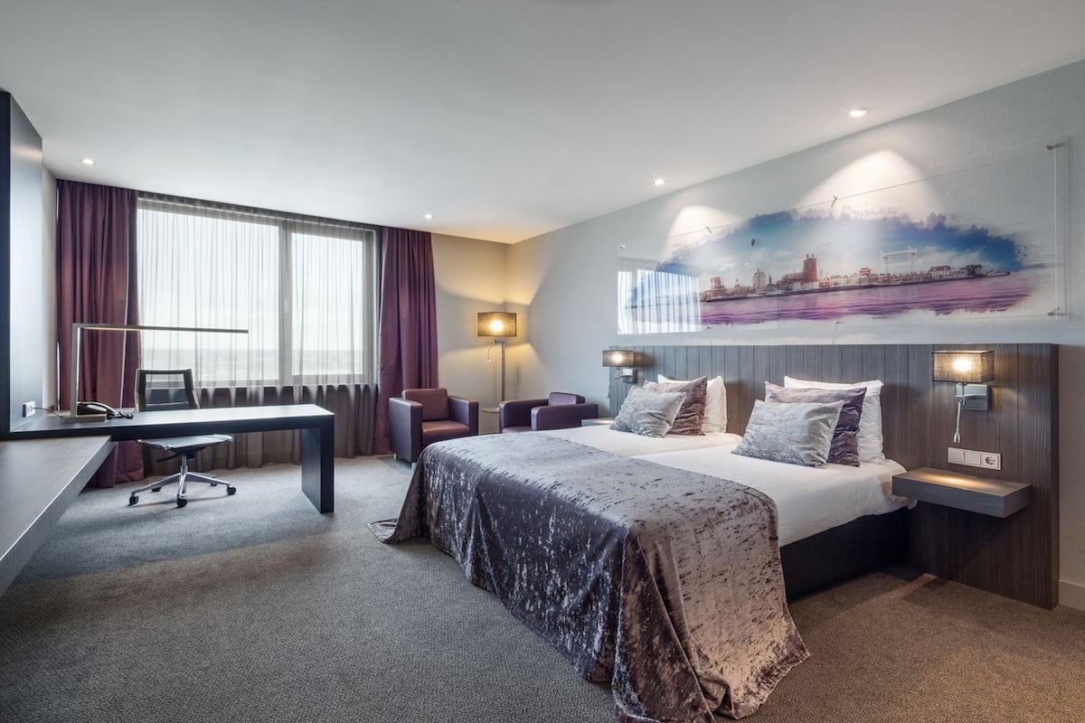 Hotellihuone, jossa on sänky, työpöytä, tuoleja ja seinällä kaupunkimaisemaa esittävä seinämaalaus.