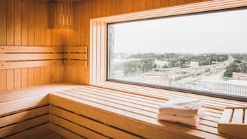 Una sauna con bancos de madera y un amplio ventanal que ofrece vistas de un paisaje urbano.