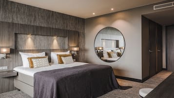 Ett modernt hotellrum med en stor säng, två sängbord med lampor, en rund spegel på väggen och en mörkfärgad matta.