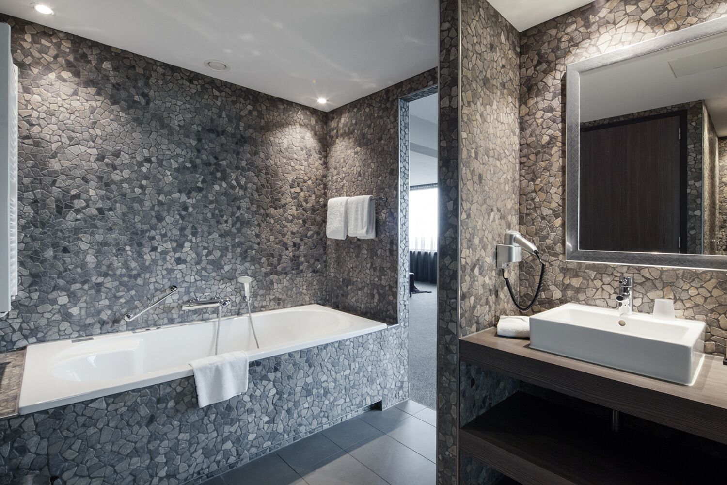 A modern bathroom with a stone wall, a bathtub, a sink, and a mirror.