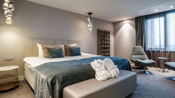 A modern hotel room with a large bed, a seating area, and a view of the city.