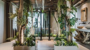 Een modern interieur met een glazen wand, houten balken en diverse planten.