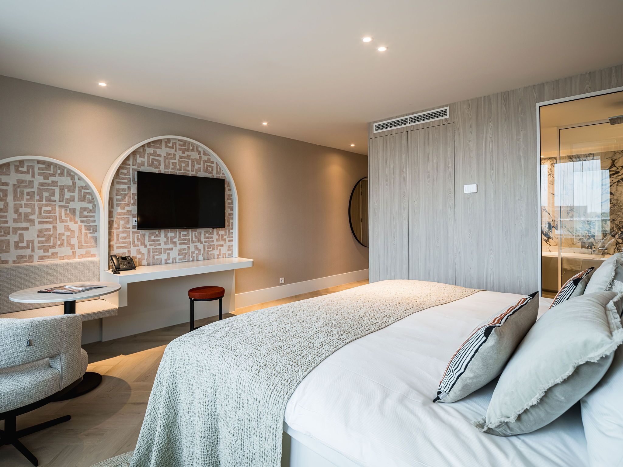 Een moderne hotelkamer met een groot bed, een bureau met een stoel, een flatscreen televisie en een zithoek met een gestreept behang.