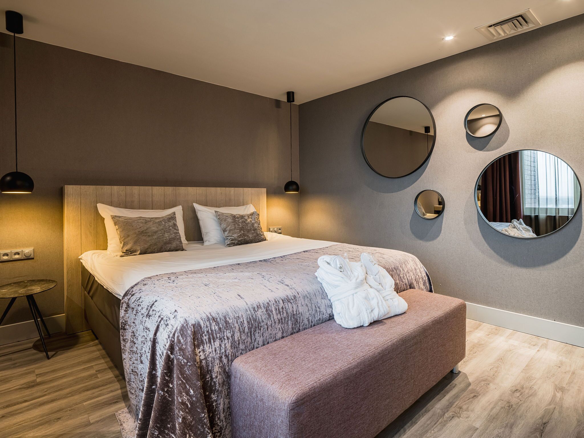 Een moderne slaapkamer met een groot bed, een ronde spiegel en een klein rond tafeltje.