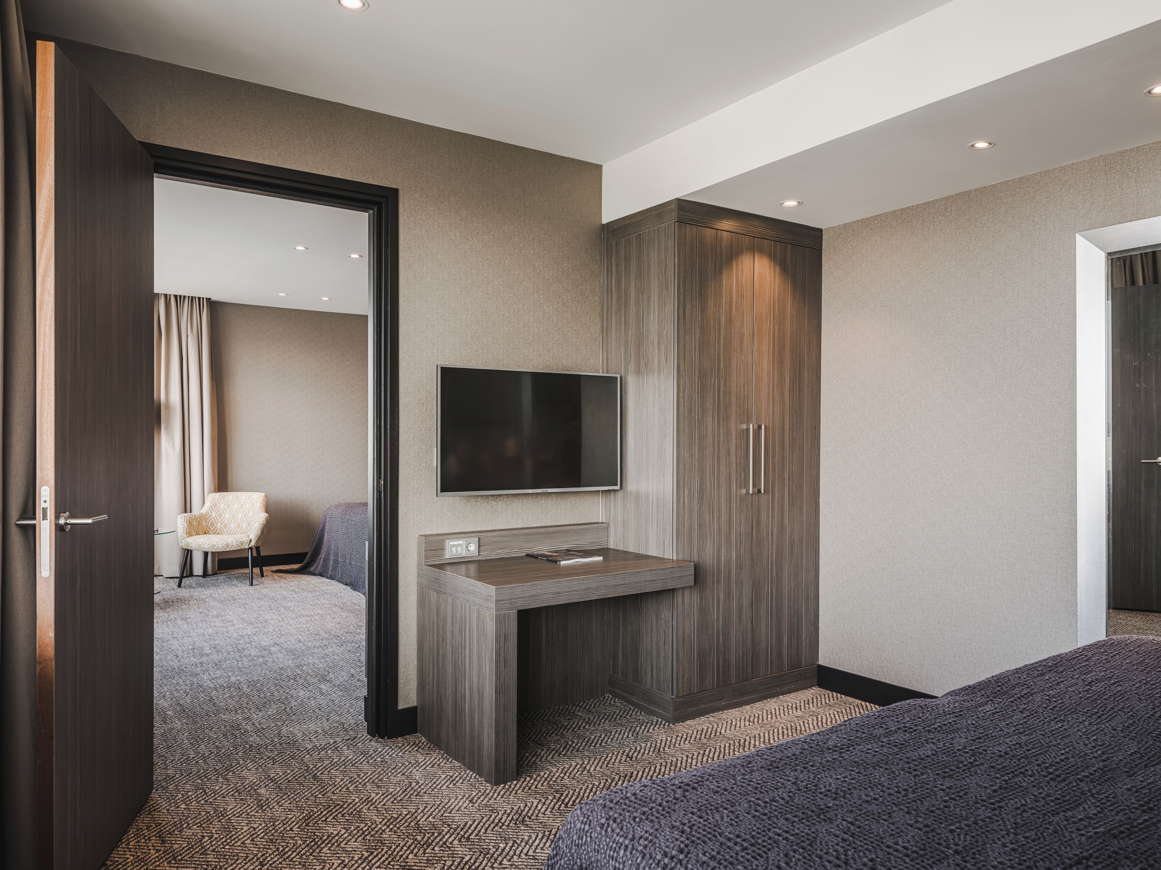 Una habitación de hotel moderna con una cama grande, un escritorio empotrado, un televisor de pantalla plana, un armario y una alfombra estampada.