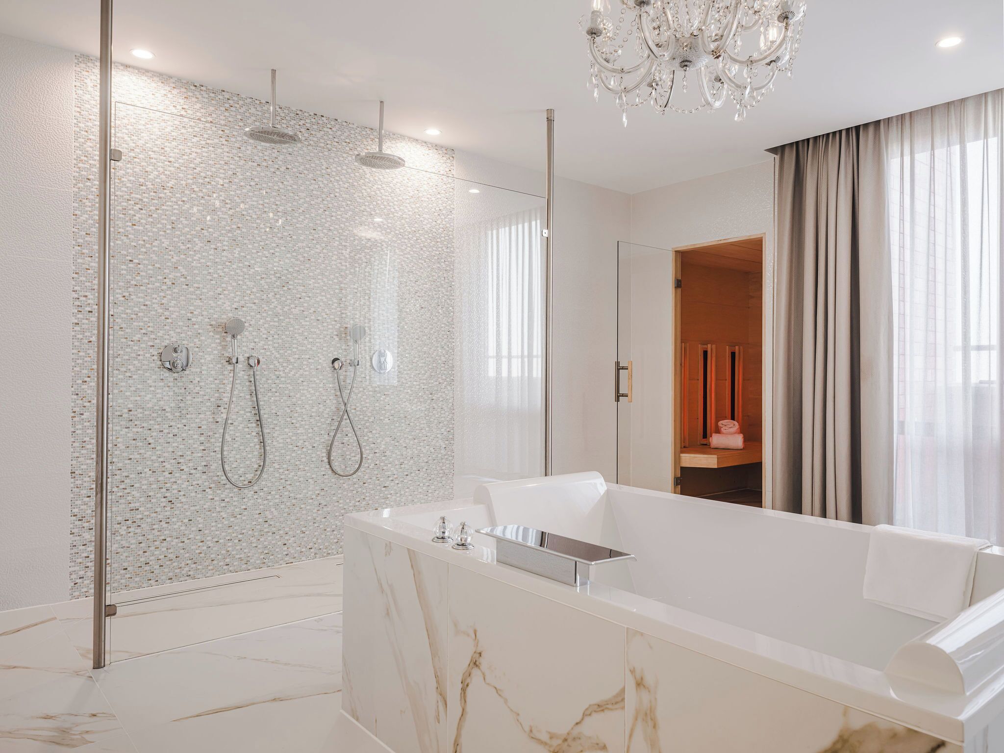 Un baño moderno con una bañera grande, cabina de ducha de vidrio y una araña.