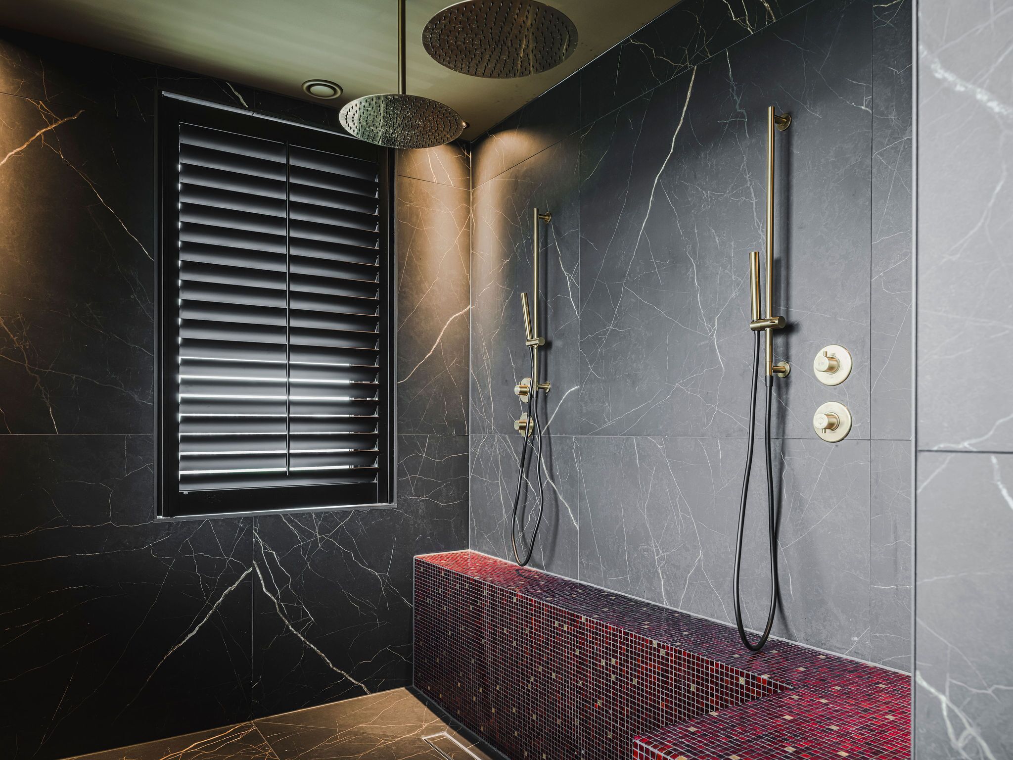 A modern bathroom with a black marble wall, a red mosaic bench, and a window with blinds.