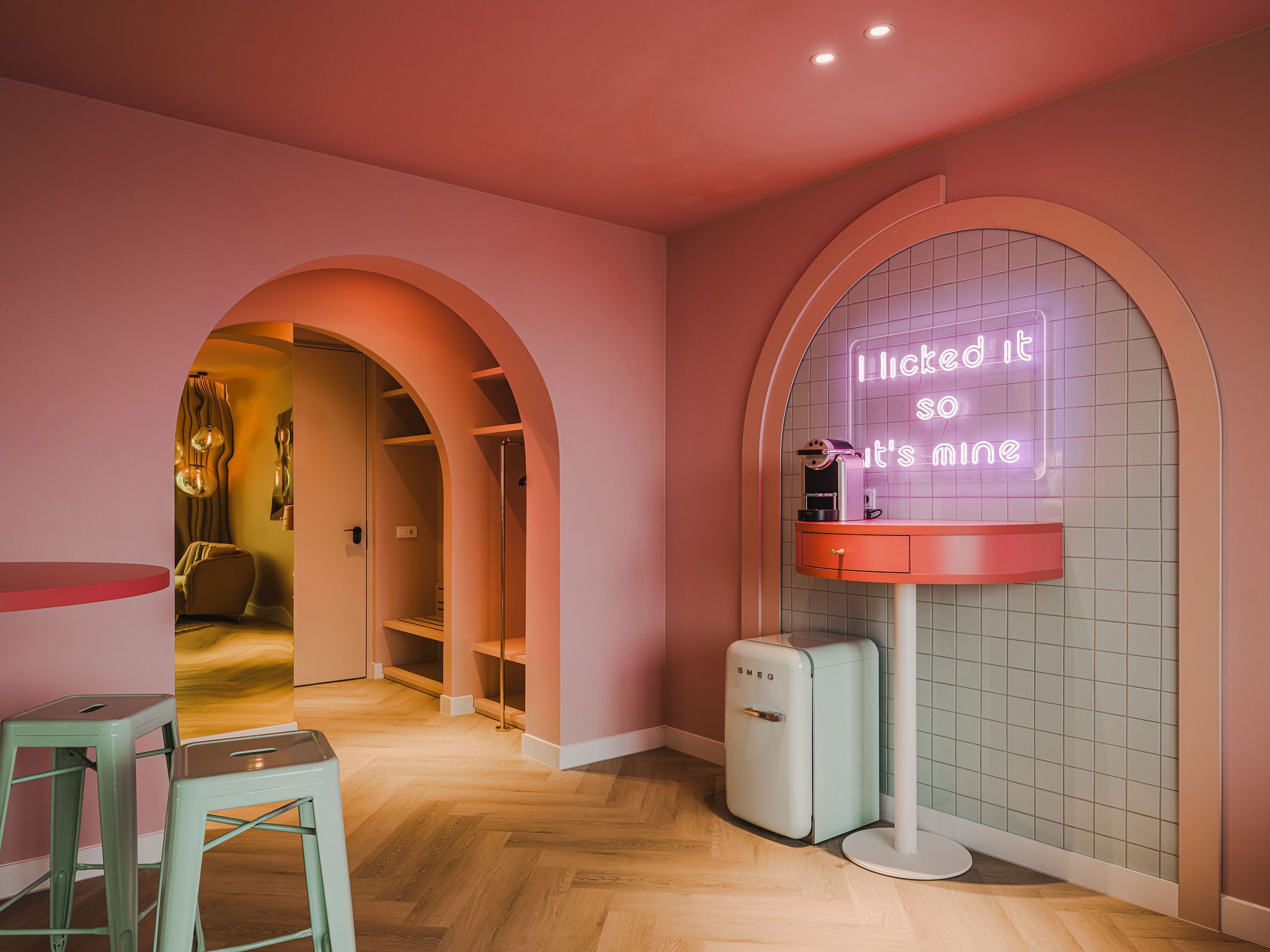 A pink-themed room with a neon sign, a vintage-style refrigerator, and a stool.