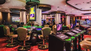 Ein Casino mit Roulette-Tischen, Spielautomaten und einem großen Bildschirm, der ein Spiel zeigt.