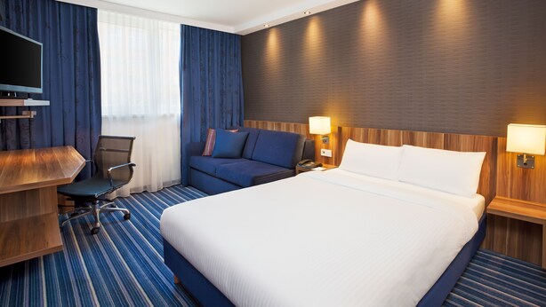 Una habitación de hotel con una cama grande, un escritorio con una silla, un televisor y un sofá.