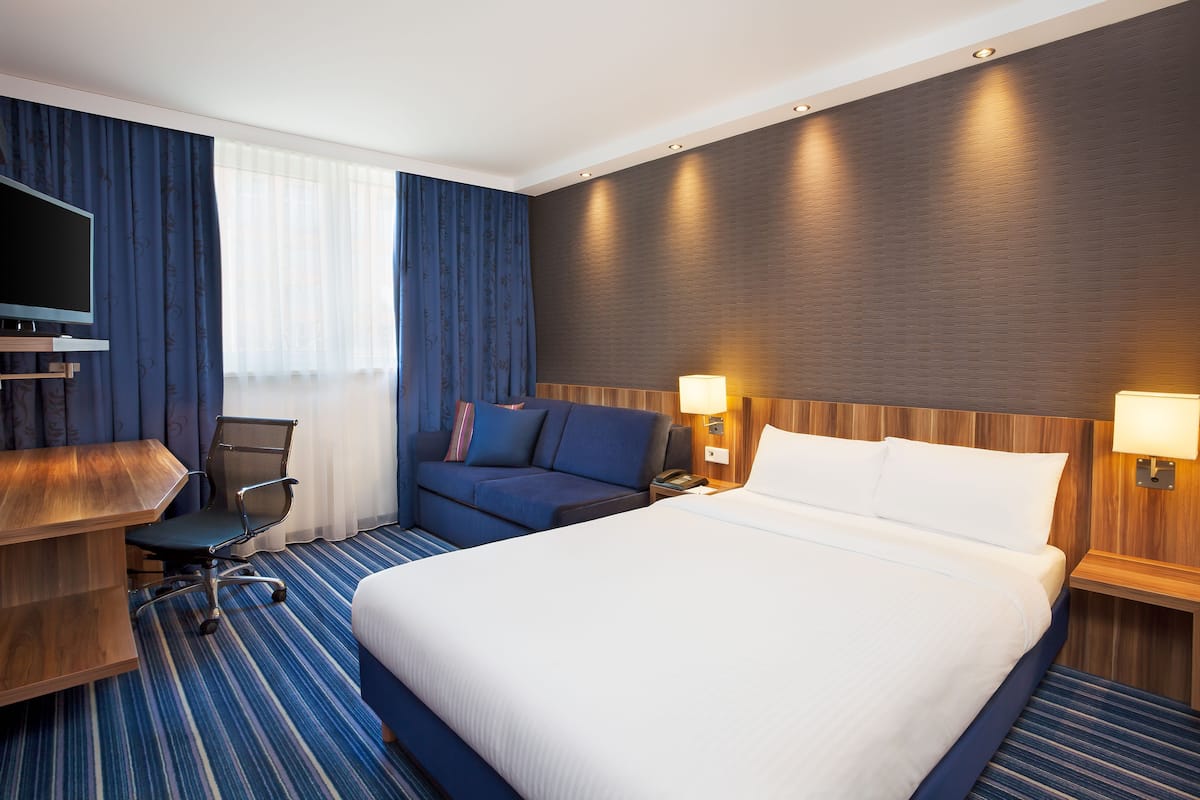 A hotel room with a large bed, a desk with a chair, a TV, and a sofa.