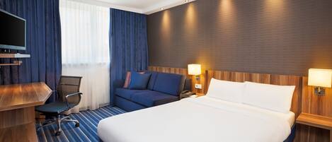 A hotel room with a large bed, a desk with a chair, a TV, and a sofa.